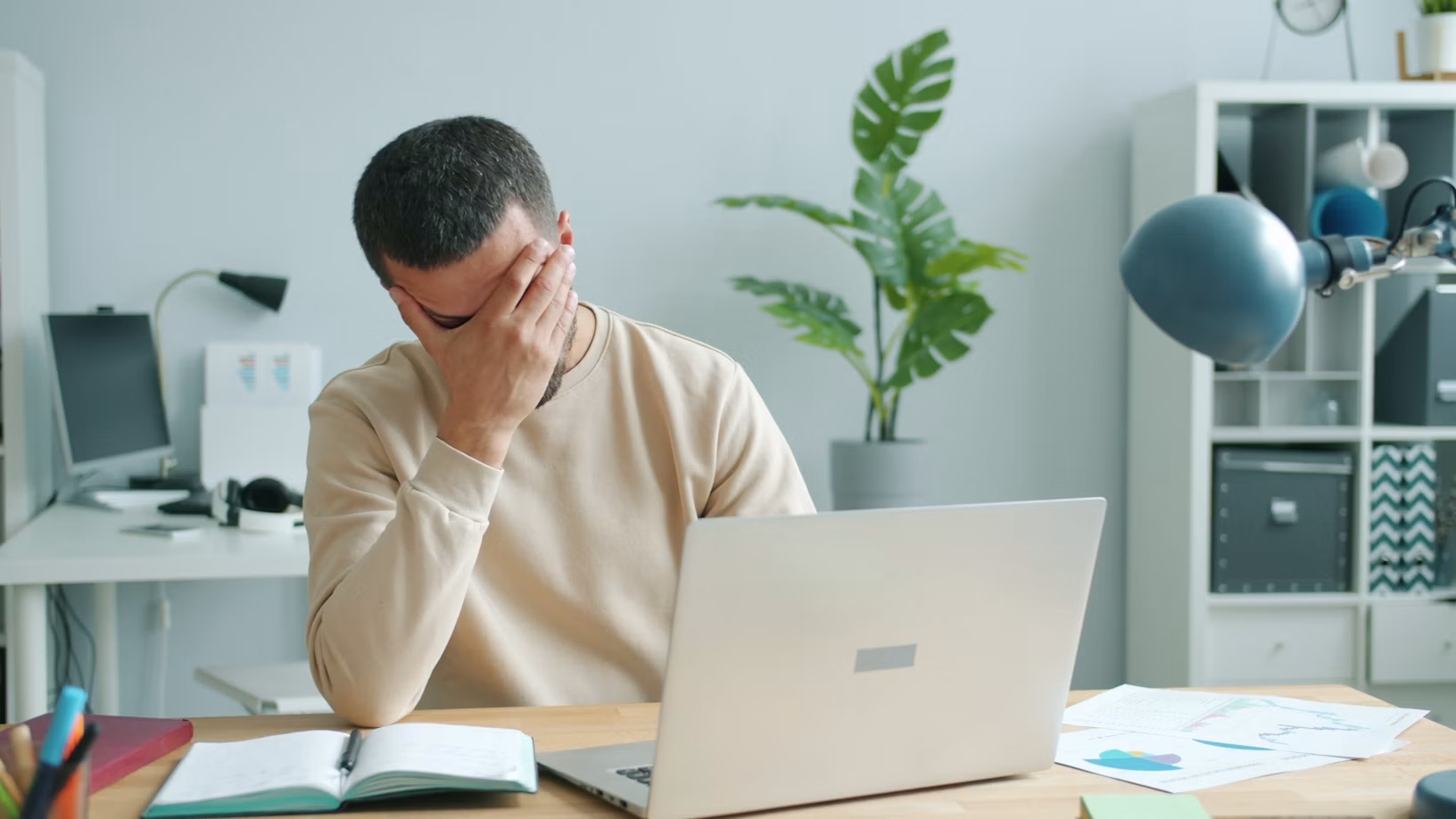 a man covering his face in front of a laptop